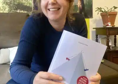 Susanne Füller sitzt auf einer Couch und hält ihr Buch mit dem Titel „Dualseelen“ in der Hand, auf dessen Cover sich eine Illustration befindet.