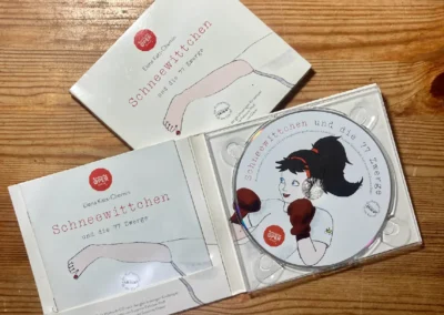 CD mit dem Titel „Schneewittchen und die 77 Zwerge“ mit einem Cover, das eine Figur mit Boxhandschuhen zeigt. Die Hülle liegt offen auf einem Holztisch.