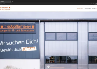 Außenansicht des Gebäudes der Sobotta IT GmbH mit einem Rekrutierungsschild in deutscher Sprache: „Wir suchen Dich! Bewirb dich JETZT!“ Hinweis auf einen Aufruf zur Einreichung von Bewerbungen.