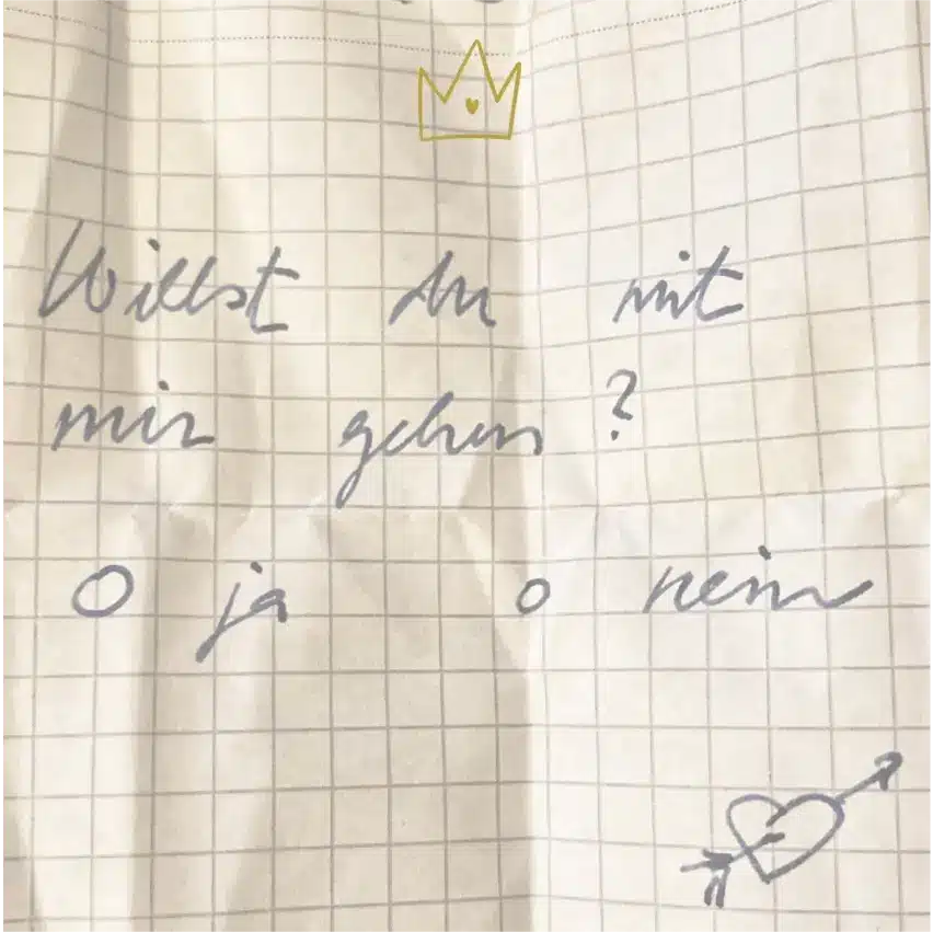Ein handgeschriebener Zettel auf Millimeterpapier fragt auf Deutsch: "Willst du mit mir gehen? O ja O nein" ("Möchtest du mit mir ausgehen? Ja oder nein"). Darauf sind eine Krone und ein Herz mit einem Pfeil gezeichnet.