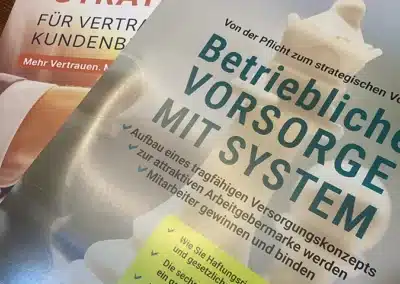 Zwei deutsche Broschüren liegen übereinander auf einem Holztisch. Eine Broschüre wirbt für "Betriebliche Vorsorge mit System", die andere für "7 clevere Strategien für Vertrieb und Kundenbindung".